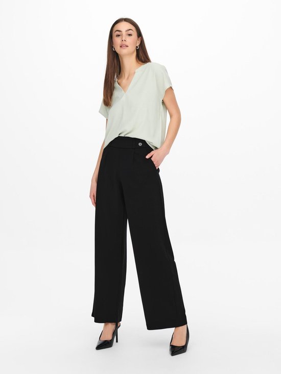 Model draagt zwarte wijde broek met hoge taille en knopen.