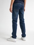 Jongen in een donkerblauwe t-shirt en jeans, staand met de rug naar de camera, met witte sneakers.