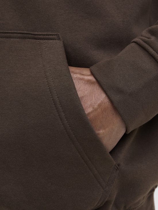Close-up van een bruine hoodie met een ingezette hand in de steekzak. De stof is katoen.