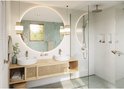 Badkamer met ronde spiegel met verlichting, dubbele wastafel en douche.