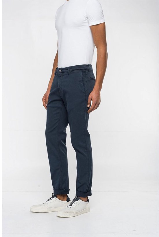 Man met donkerblauwe chino broek, omgeslagen broekspijpen en witte sneakers, zijaanzicht.