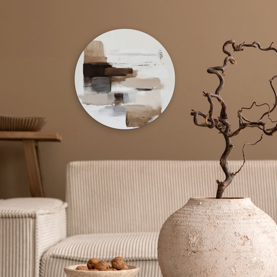 Ronde muurdecoratie met bruine en beige penseelstreken, hangend aan een bruine muur boven een bank.