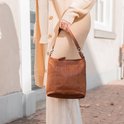 Vrouw met bruine leren schoudertas, gedragen over de schouder, met een beige gebreide cardigan.