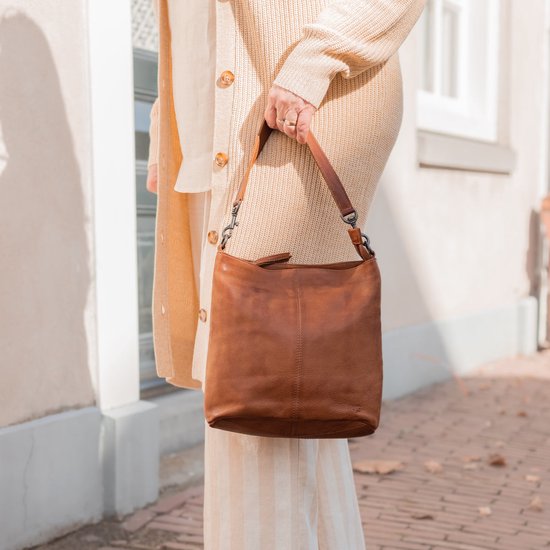 Vrouw met bruine leren schoudertas, gedragen over de schouder, met een beige gebreide cardigan.