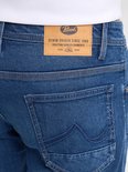 Achterkant van de blauwe spijkerbroek met een bruin leren merklabel waarop staat: Petrol Denim Driven Since 1989.