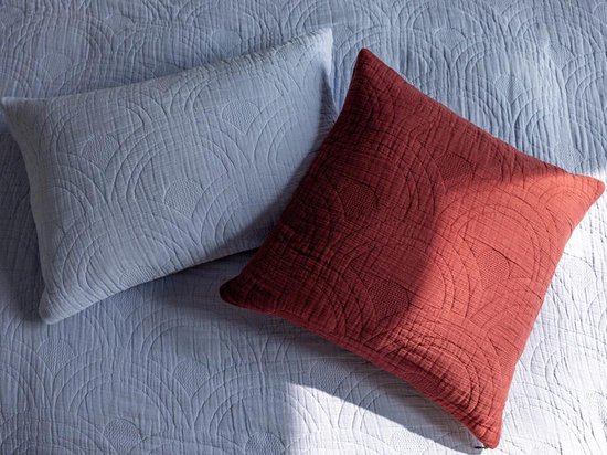 Twee kussens, één lavendelblauw en één roodbruin, op een lavendelblauwe spreideken met rond patroon.