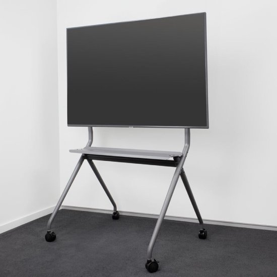Support TV gris avec un grand écran noir, positionné dans un coin de pièce sur une moquette grise.