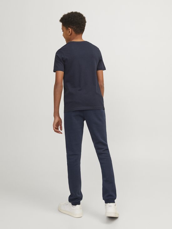 Jongen van achteren gezien, in een marineblauwe joggingbroek en bijpassend T-shirt, met witte sneakers.
