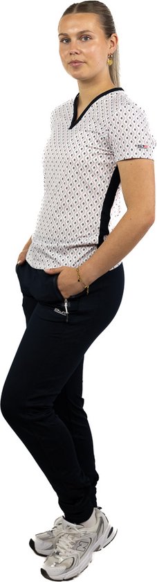 Model draagt een wit T-shirt met zwarte stippen en een donkerblauwe sportbroek, met de handen in de zakken.