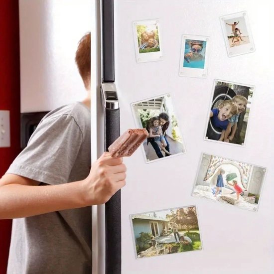 Een jongen eet een ijsje terwijl hij naar magnetische fotolijstjes op een koelkast kijkt.