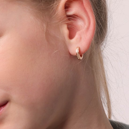 Gouden oorring met kristallen, gedragen door een meisje.