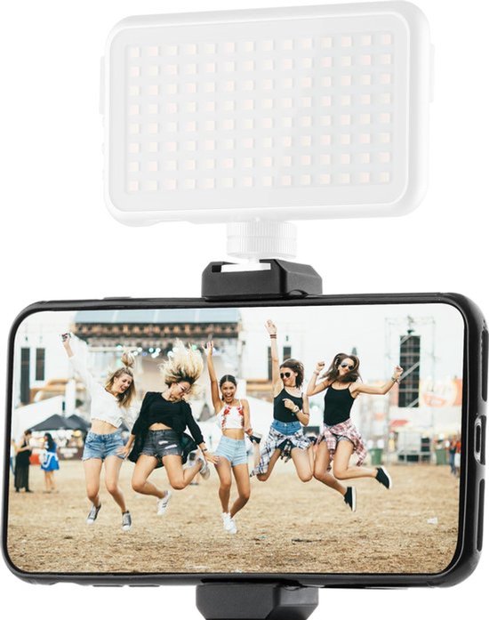 Een smartphone met een foto van vijf springende meisjes op een festival, bovenop een MOJOGEAR LED lamp en een statief.