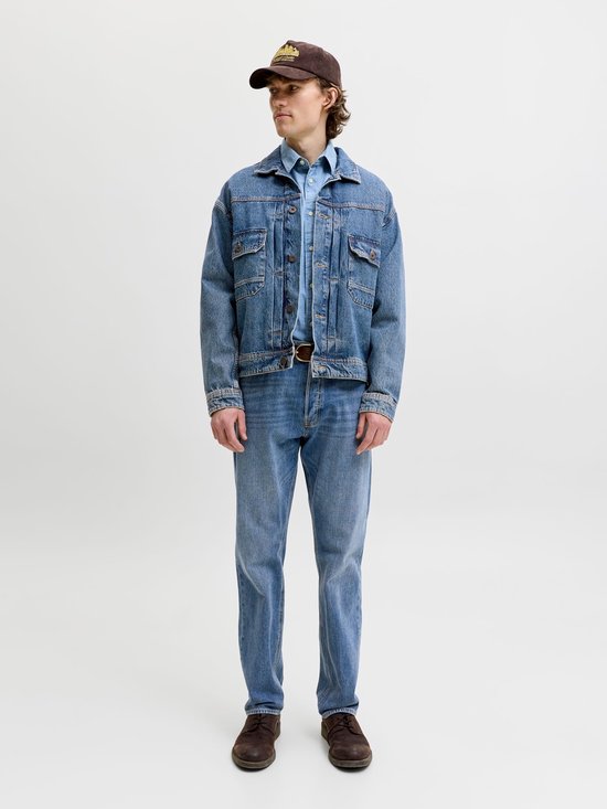Man in een complete denim outfit: spijkerjasje, lichtblauw overhemd en rechte jeans. Bruine pet en schoenen.