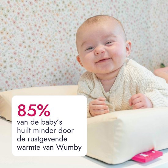 Een blije baby met een gebreide trui ligt op een zandkleurig aankleedkussen. 85% van de baby's huilt minder.