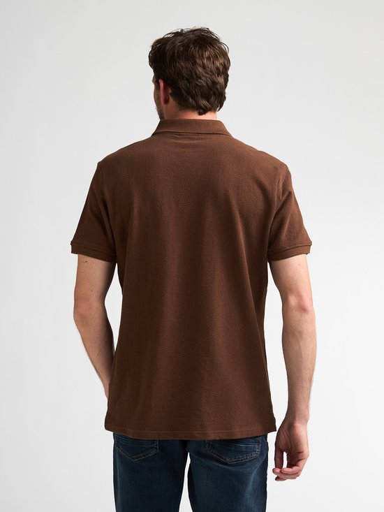 Man van achteren gezien, draagt een bruin katoenen poloshirt met korte mouwen.
