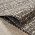 Bruin rond vloerkleed met abstract patroon. De rand is afgewerkt met een donkerbruin feston.