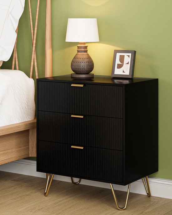 Zwart nachtkastje met 3 laden, gouden pootjes en gouden handgrepen, naast een bed.