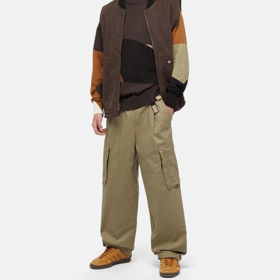 Man in een gebreide trui met gekleurde blokken, een bruine bodywarmer en een beige cargobroek.