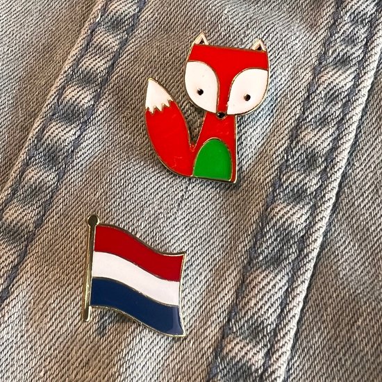 Emaille pin van een vosje met rode vacht, witte snuit en staartpunt, en groene buik. Naast een Nederlandse vlag pin.