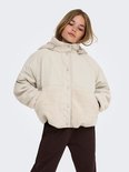 Meisje staat met handen in de zakken, draagt een beige teddy jas, bruine joggingbroek.