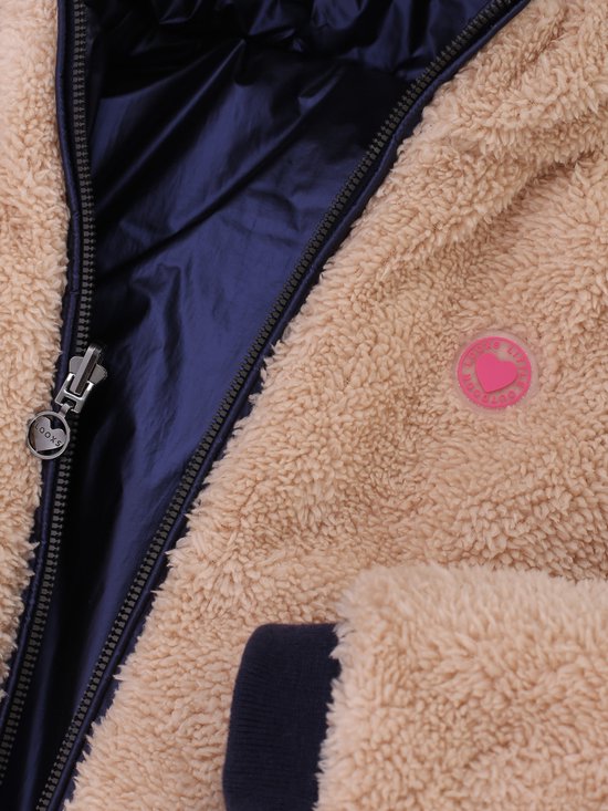 Sluiting van een lichtbruine teddy jas met een glanzende donkerblauwe voering en een roze hartvormig logo.