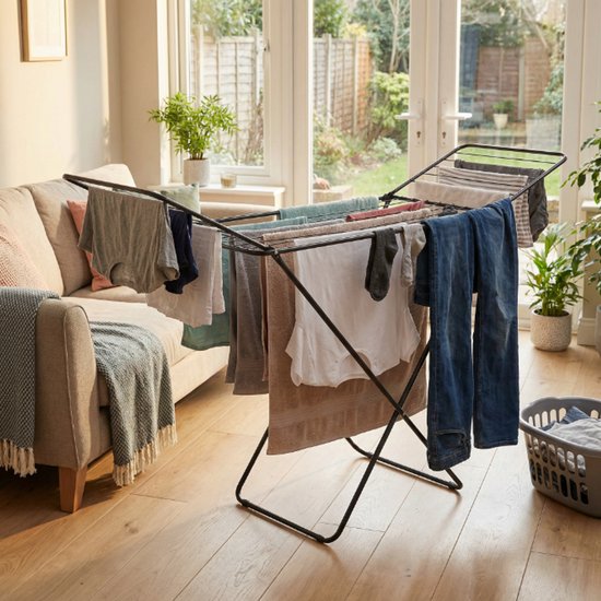 Zwart droogrek met vleugels, beladen met kleding, in een woonkamer.