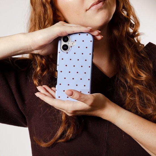 Vrouw met lang rood krullend haar omringt een lichtblauwe telefoonhoes met bruine stippen met haar handen.