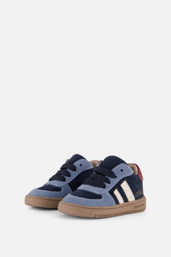 Paar donkerblauwe en lichtblauwe suède sneakers met witte strepen en rode hielen.