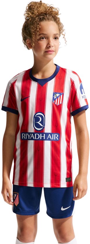 Meisje in rood-wit gestreept Atlético Madrid thuisshirt. Blauwe kraag en mouwboorden, logo's op shirt.