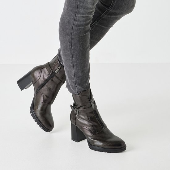 Dames draagt donkerbruine leren enkellaarsjes met rits en gesp, onder grijs aansluitende jeans