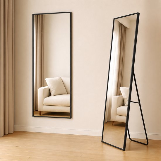 Twee staande spiegels met zwart frame in een woonkamer, één leunend tegen de muur en de ander op een standaard.