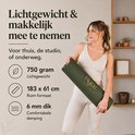 Vrouw in beige outfit houdt een opgerolde donkergroene yogamat met gouden print vast. Details: 750 gram, 183x61cm, 6mm dik.