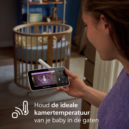 Vrouw houdt babyfoon vast met waarschuwing voor hoge kamertemperatuur op het scherm.