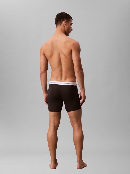 Man met donkere Calvin Klein boxer briefs met witte tailleband met logo, achterkant zichtbaar.