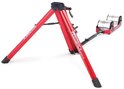 Een opvouwbare rode Fietstrainer met zilveren rollen,merk Feedback Sports.