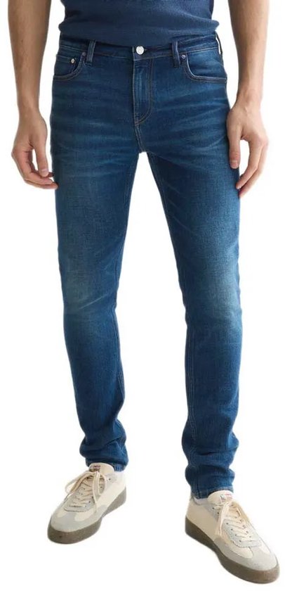 Man in een skinny fit spijkerbroek met een medium blauwe wassing. De broek heeft een lichte slijtage.