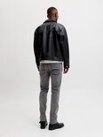Achterkant man met zwarte leren jas, wit T-shirt en grijze jeans.