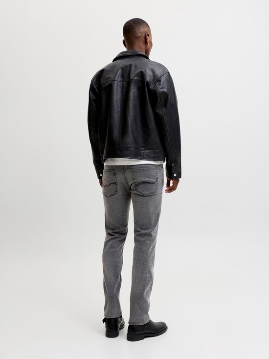 Achterkant man met zwarte leren jas, wit T-shirt en grijze jeans.