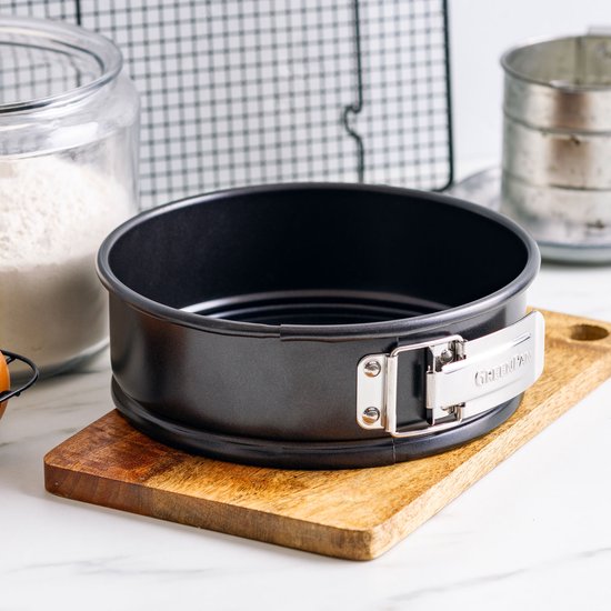 Zwarte ronde springvorm met zilverkleurige gesp en 'GREENPAN' logo, op houten plank.