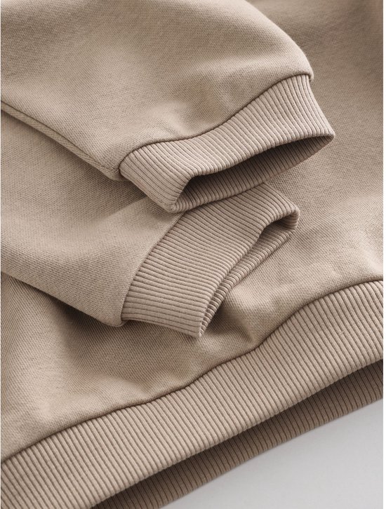 Close-up van de geribbelde boorden aan de mouwen en onderkant van een naturelkleurige sweater.