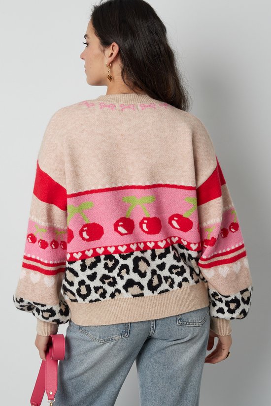 Model draagt beige gebreide sweater met ronde hals. Op de rug een roze baan met kersenprint, leopardprint en hartjes.