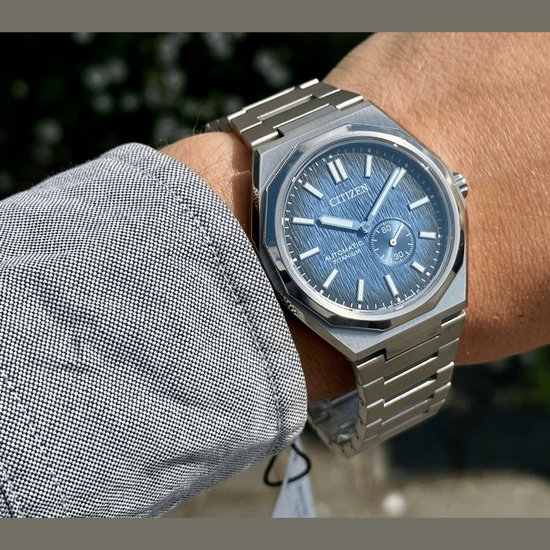 Gedetailleerde foto van zilverkleurig Citizen horloge met blauwe wijzerplaat met textuur, gedragen om pols.
