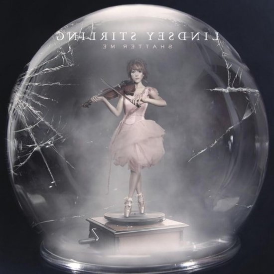 Violiste in roze ballerina-outfit op draaiplateau in gebroken glazen bol, met tekst 'LINDSAY STIRLING SHATTER ME'.