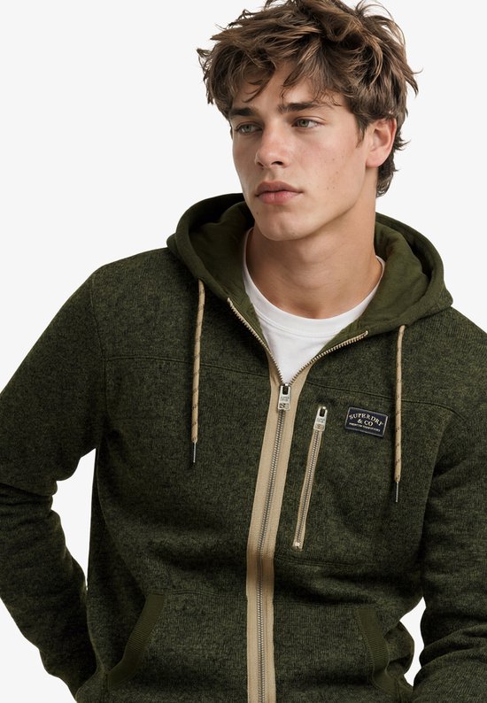 Model in olijfgroene, gemêleerde fleece hoodie met beige rits en Superdry & Co-embleem.