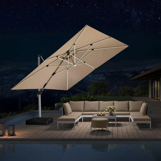 Rechthoekige, beige zweefparasol met ingebouwde LED-verlichting boven een modulaire loungebank en een zwembad. De parasol is 's avonds verlicht.