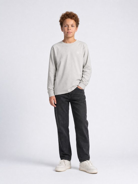 Jongen met krullend rood haar in een lichtgrijze longsleeve met subtiel logo en zwarte jeans.