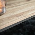 Detail van het licht houten tafelblad met een grof patroon. Glazen windlicht met brandende kaars.