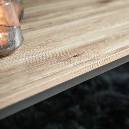 Detail van het licht houten tafelblad met een grof patroon. Glazen windlicht met brandende kaars.