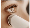 Close-up van een vrouwenoog en een witte metalen applicator, die de huid onder het oog streelt.