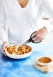 Zwarte keukenschaar snijdt kimchi in een witte kom met gestampte rode pepers ernaast.